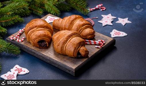 Crispy chocolate croissant with Christmas decorations on wooden cutting board on dark concrete background. Crispy chocolate croissant with Christmas decorations on wooden cutting board
