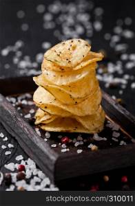 Crispy delicious pepper potato crisps chips snack on dark wooden board and salt