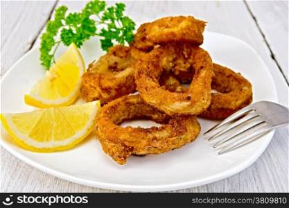 Crispy fried calamari rings on a plate with slices of lemon and parsley on a wooden boards background