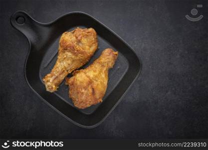 crispy fried chicken drumstick in black skillet pan on the dark tone texture background with copy space for text, top view, flat lay