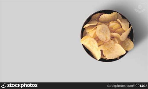Crispy potato chips in a black ceramic tray on a grey background, top view.