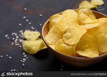 Crispy potato chips in bowl with salt