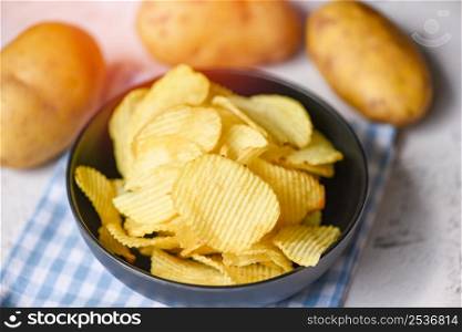 Crispy potato chips on the kitchen table and fresh raw potatoes on wooden background, Potato chips snack on bowl
