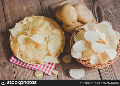 Crispy potato chips on the kitchen table and fresh raw potatoes on wooden background, Potato chips snack on bowl and plate
