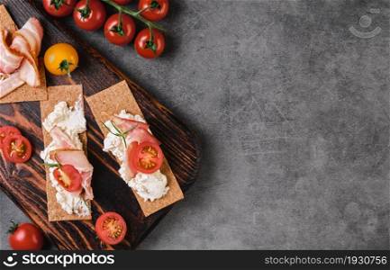 Crispy rye crispbreads with cream cheese, tomatoes and bacon. The idea of bruschetta for a healthy breakfast with a source of fiber and protein. Layout on the table with copy space.