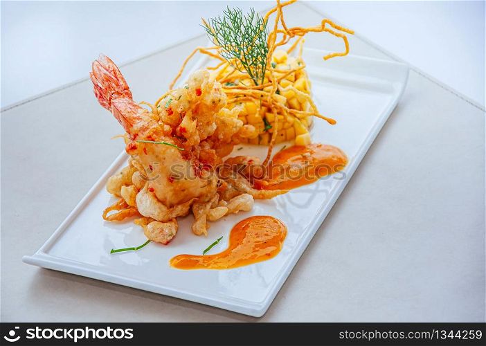 Crispy spicy deep fried tiger prawn with mango salsa and hot chilli thousand island sauce on white plate