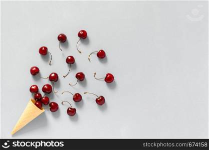 Crispy waffle ice cream cone with scattered red ripe sweet cherries. Still life on grey background. Copy space, Flat lay, Top view, greeting card.. Crispy waffle ice cream cone with scattered red ripe sweet cherries. Still life on grey background. Copy space, Flat lay, Top view, greeting card