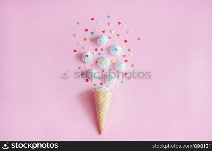 Crispy waffle ice creame cone with scattered white twisted meringues and with confectionary. Still life on pink background. Flat lay, Top view. Greeting card Concept