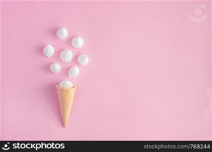Crispy waffle ice creame cone with scattered white twisted meringues on pink background