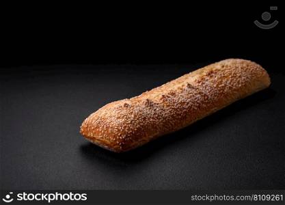 Crispy wheat flour baguette with sesame seeds on a wooden cutting board on a dark concrete background
