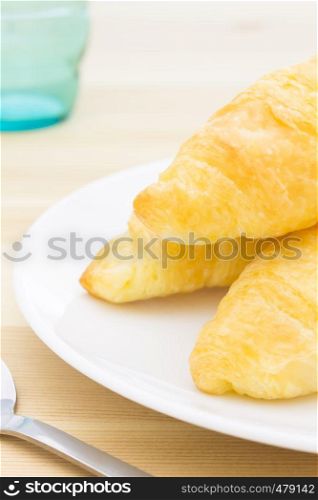 Croissant or bread or bakery on white dish on wood table with spoon and glass portrait view