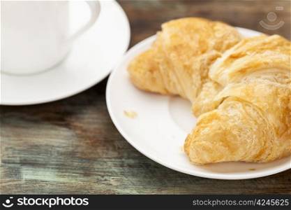 croissant roll with espresso coffee cup on grunge painted wooden table, shallow depth of field