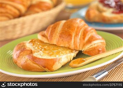 Croissant with butter and orange jam (Selective Focus, Focus on the front of the orange jam on the croissant and on the wooden spoon)