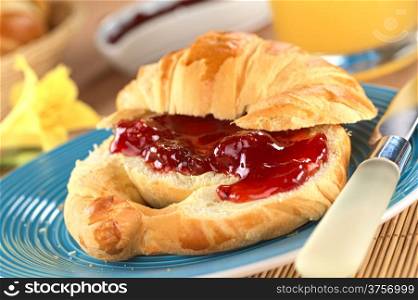 Croissant with butter and strawberry jam (Selective Focus, Focus on the big strawberry piece in the front)