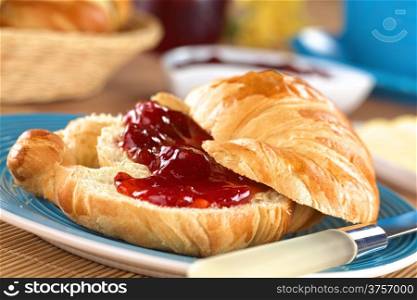 Croissant with butter and strawberry jam (Selective Focus, Focus on the front of the upper croissant half and the strawberry piece in the middle of the image)