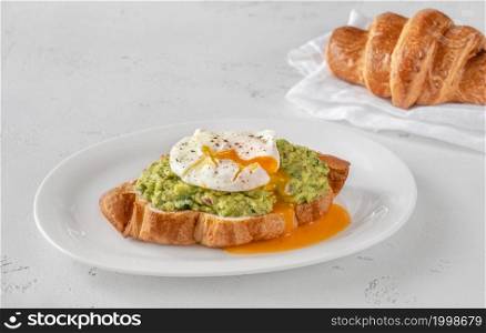 Croissant with guacamole and poached egg on the serving plate