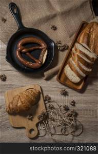 Croissants and fresh pretzels with baguette bread, placed on a tray and a wooden chopping board, placed on a wooden table from the top view.
