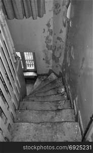Crooked wooden staircase and peeling paint wall in abandoned house. Black and white.