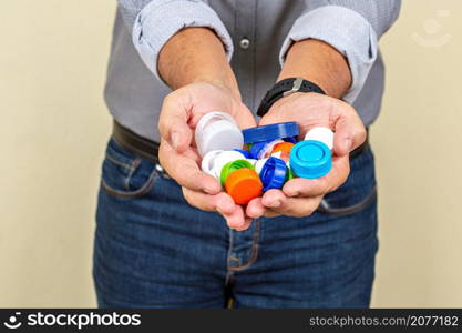 Crop anonymous male showing heap of colorful plastic lids prepared for recycling while standing on beige background. Crop man with pile of plastic caps