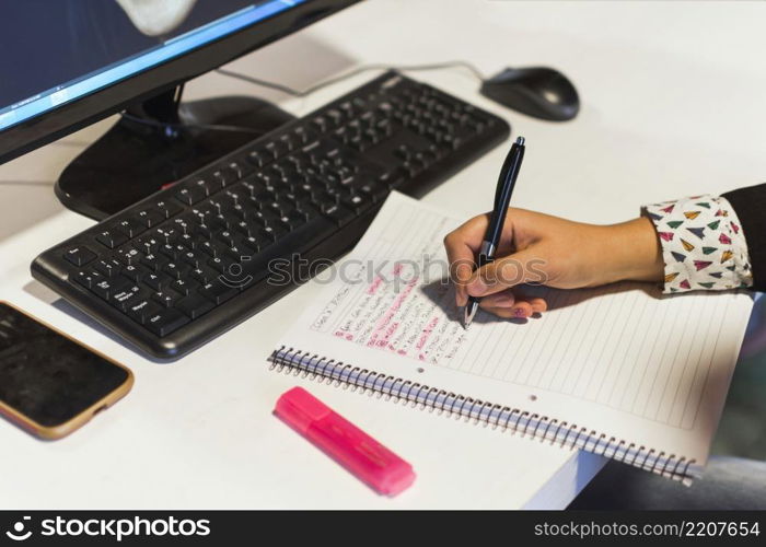 crop hand writing notebook near computer