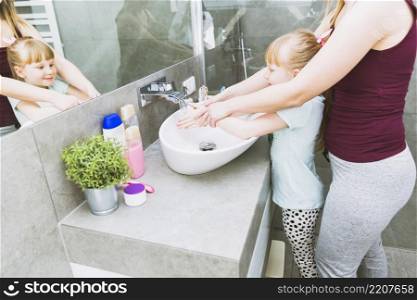 crop mother helping daughter wash hands