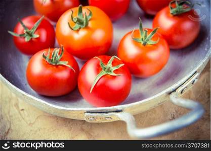 Crop of young tomatoes in a metal skillet, rustic style with vintage purple toning