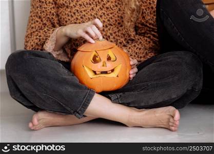Crop view of adult woman sitting on the floorat home with carved halloween pumpkin. pumpkin jack-o-lantern, indoors. Trick or trunk. Happy Halloween day. selective focus.. Crop view of adult woman sitting on the floorat home with carved halloween pumpkin. pumpkin jack-o-lantern, indoors. Trick or trunk. Happy Halloween day. selective focus