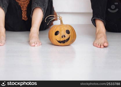 Crop view of young man and woman sitting on the floor at home with halloween pumpkin. pumpkin jack-o-lantern, indoors. Trick or trunk. Happy Halloween day. Crop view of young man and woman sitting on the floor at home with halloween pumpkin. pumpkin jack-o-lantern, indoors. Trick or trunk. Happy Halloween day.