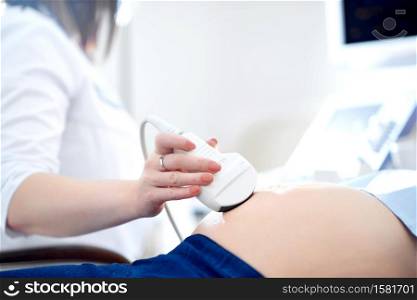 Cropped close up of an ultrasound scanner in hands of doctor examining her pregnant patient copyspace technology modern medicine healthcare pregnancy diagnosing sonogram unborn motherhood concept.. Doctor performing ultrasound scanning for her pregnant patient