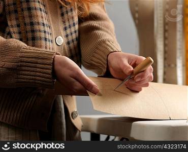 Cropped close up of young female fashion designer piercing dressmaker&acute;s pattern