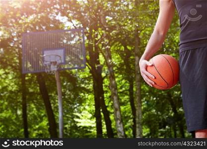 Cropped detail of young male basketball player holding ball in front of basketball hoop
