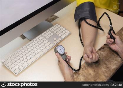 Cropped image and selective focus at female doctor or nurse?s hand using sphygmomanometer to measuring blood pressure of her patient in medical office