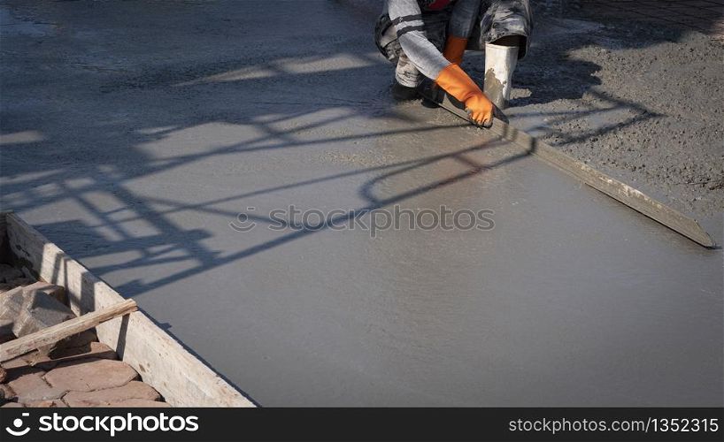 Cropped image of Asian construction worker using long triangle trowel to plastering cement on the floor in construction site