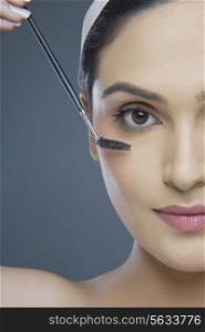 Cropped image of beautiful young woman using eyebrow tinting applicator over colored background