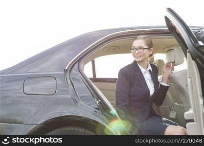 Cropped image of businessman holding car door for colleague against sky