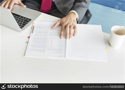 Cropped image of businessman with book and laptop at desk