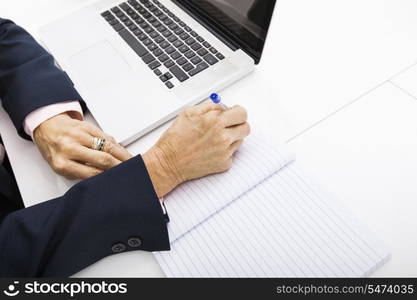 Cropped image of businesswoman with laptop writing in notebook on office desk