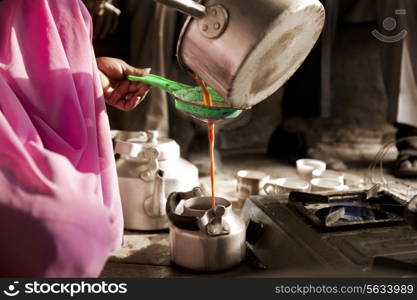 Cropped image of female vendor pouring hot streaming chai in kettle