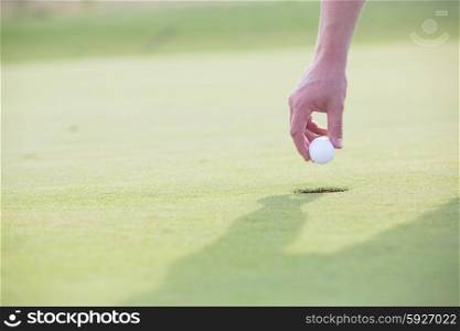 Cropped image of hand holding golf ball over cup