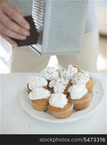 Cropped image of woman grating chocolate on cupcakes at counter