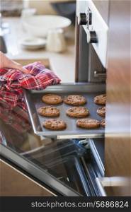 Cropped image of woman&rsquo;s hand removing cookie tray from oven in kitchen