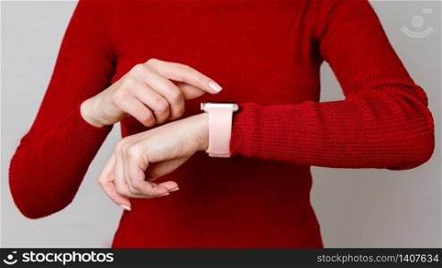 Cropped photo of woman touching, setting or using her smartwatch on her wrist, checking the time, over red turtleneck background