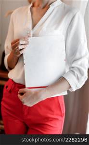 cropped photo of young woman holding a magazine with mock up. girl in a white shirt and red pants standing near the window.. cropped photo of young woman holding a magazine with mock up. girl in a white shirt and red pants standing near the window