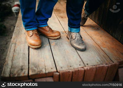 Cropped photo young legs in stylish shoes, married couple, husband and wife on a wooden bridge near lake. Rear view of couple standing on pier. Cropped photo young legs in stylish shoes, married couple, husband and wife on a wooden bridge near lake. Rear view of couple standing on pier.