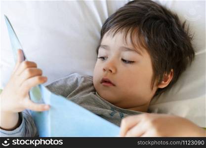 Cropped shot A happy kid lies in bed reading a book, Happy Child boy reading his favorit story book before sleep, Bed time story concept
