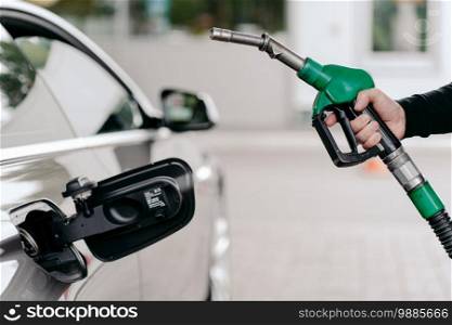 Cropped shot of mans hand pumping gasoline fuel in car at gas station. Auto being filled with petrol. Unrecognizable man holds fuel nozzel.