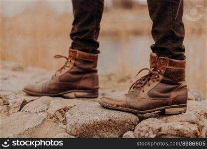 Cropped shot of unrecognizable man wears old shoes, has walk outdoor, blurred background. Boots on stones. Fashion concept