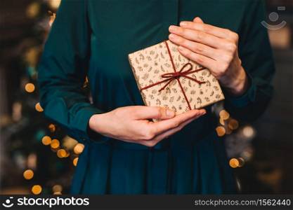 Cropped shot of unrecognizable woman in festive dress being glad to recieve christmas present from husband stand against New Year decorated fir tree. Congratulation and celebration concept