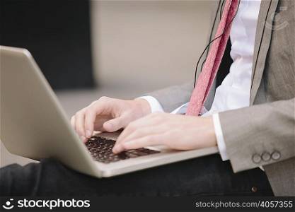 Cropped shot of young city businessman sitting on sidewalk typing on laptop