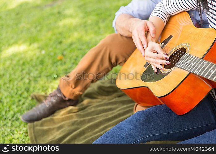 Cropped view of couple sitting on grass playing acoustic guitar